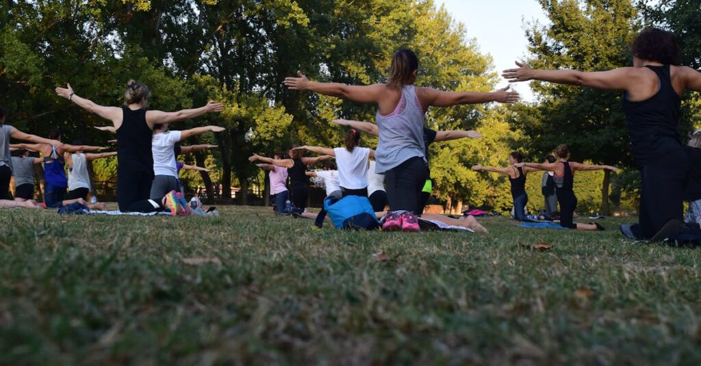 Group of adults practicing yoga outdoors in a park surrounded by trees.